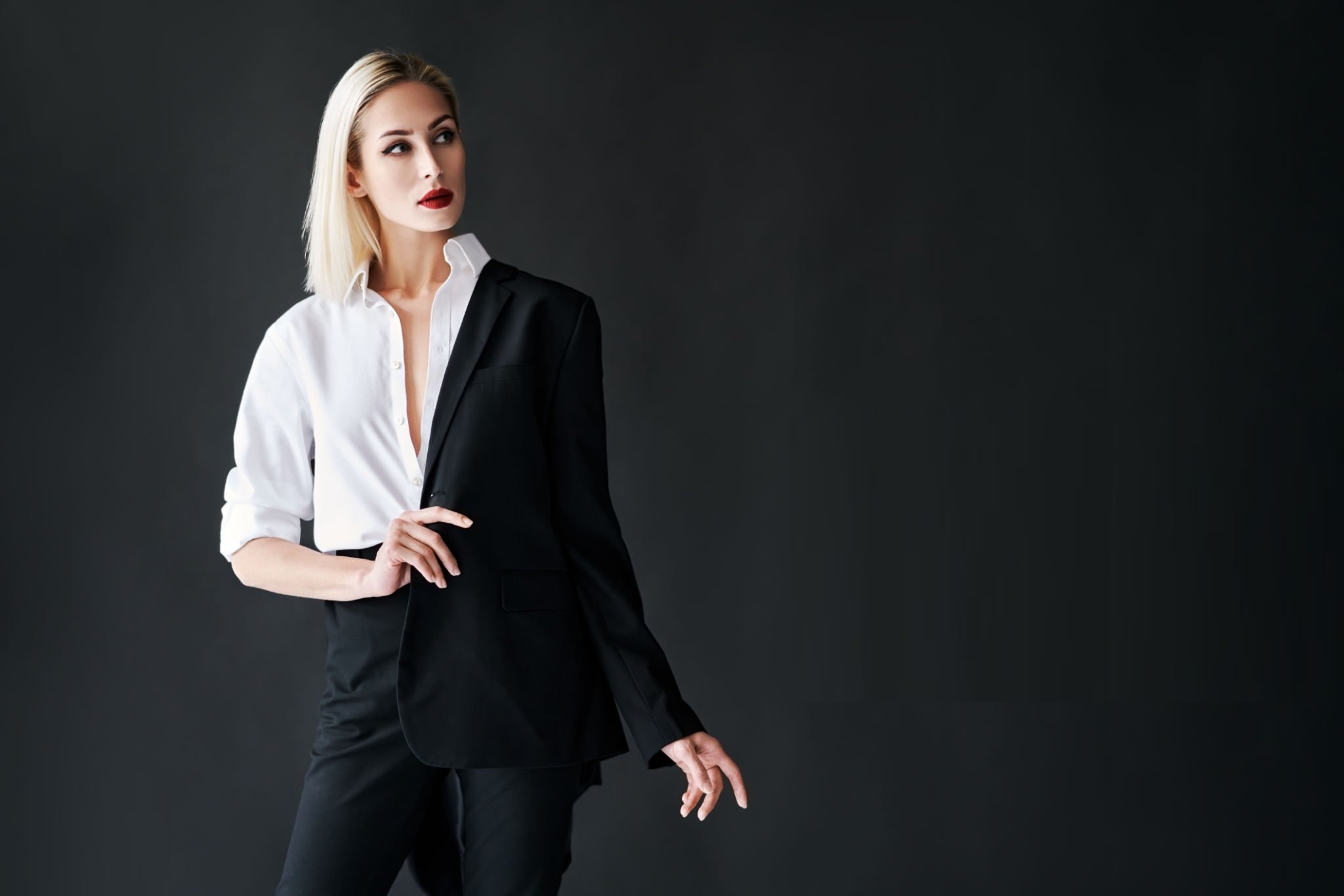 Young stylish woman wearing classic men's suit posing on black studio background with copy space. Fashion portrait of trendy female model. Black and white.